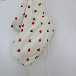 Off-white baby shorts with a red apple print, hanging on a white door.