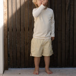 Child standing against a wooden wall with sunlight casting shadows