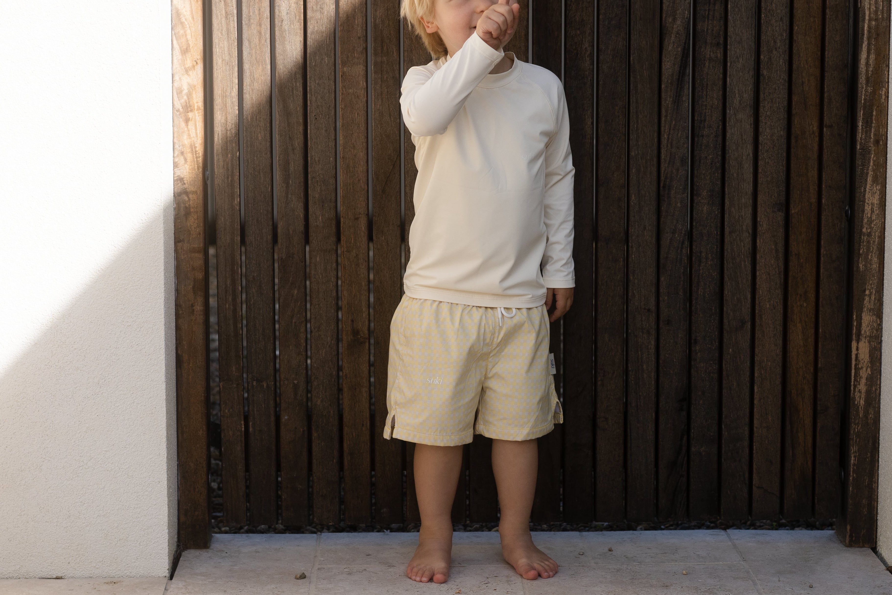 Child standing against a wooden wall with sunlight casting shadows