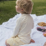 Child sitting on a blanket outdoors with a picnic setup