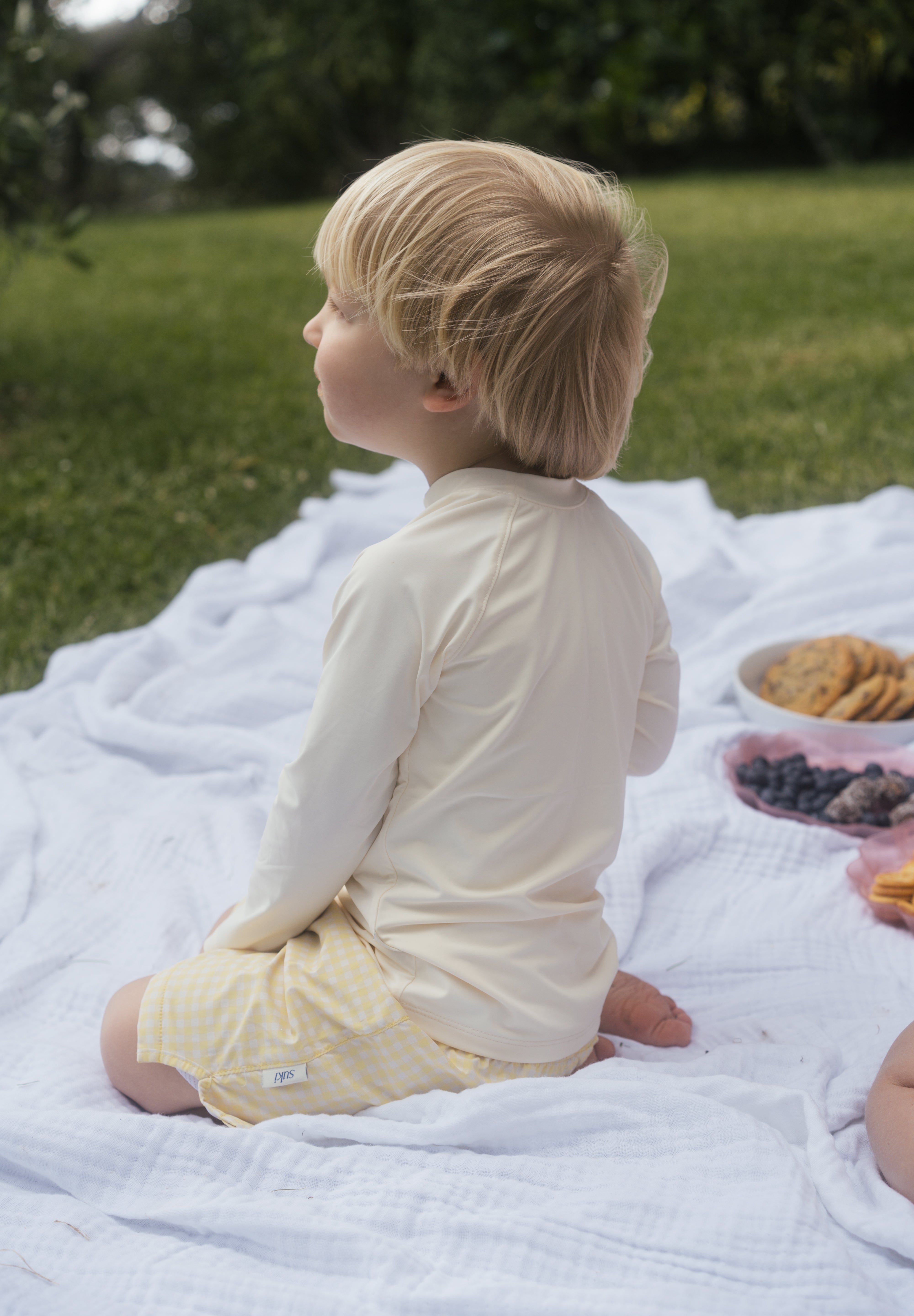 Child sitting on a blanket outdoors with a picnic setup