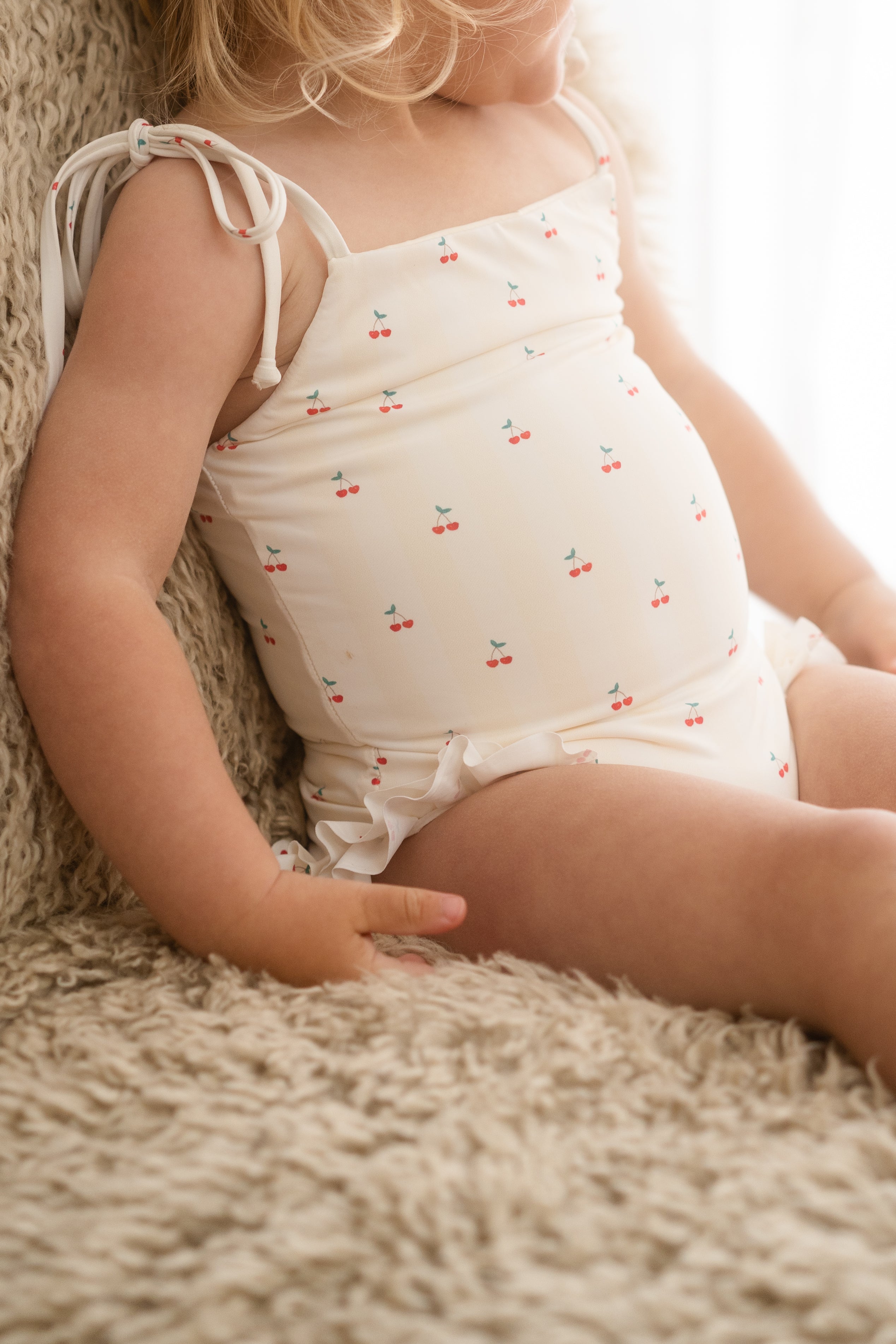 Child wearing a white romper with red cherries on a soft surface