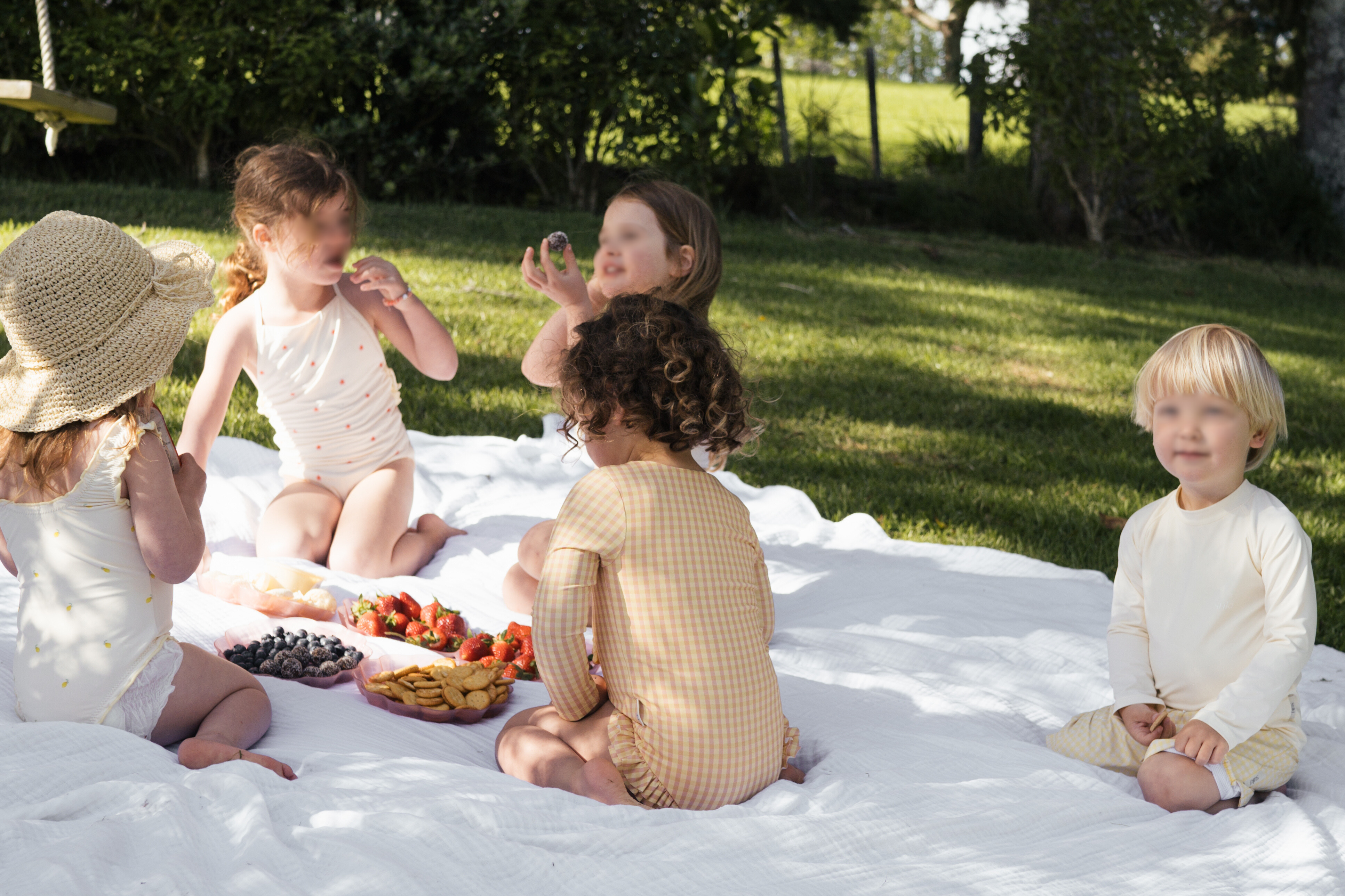 Children sitting on a blanket outdoors with fruits and a basket.